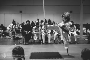 Black and white photograph of eight year old girl jumping and kicking in a karate tournament
