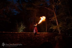 Woman wearing a dress and standing on bridge blowing fire four feet into the air above her
