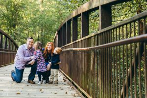 Family of four with two littles smilling and smooching on bridge in East Cobb park
