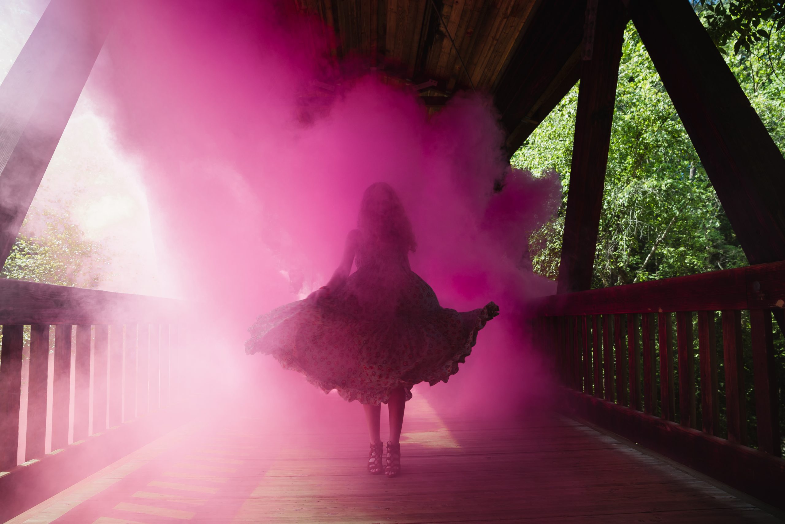 High school senior twirling in pink smoke on a covered bridge