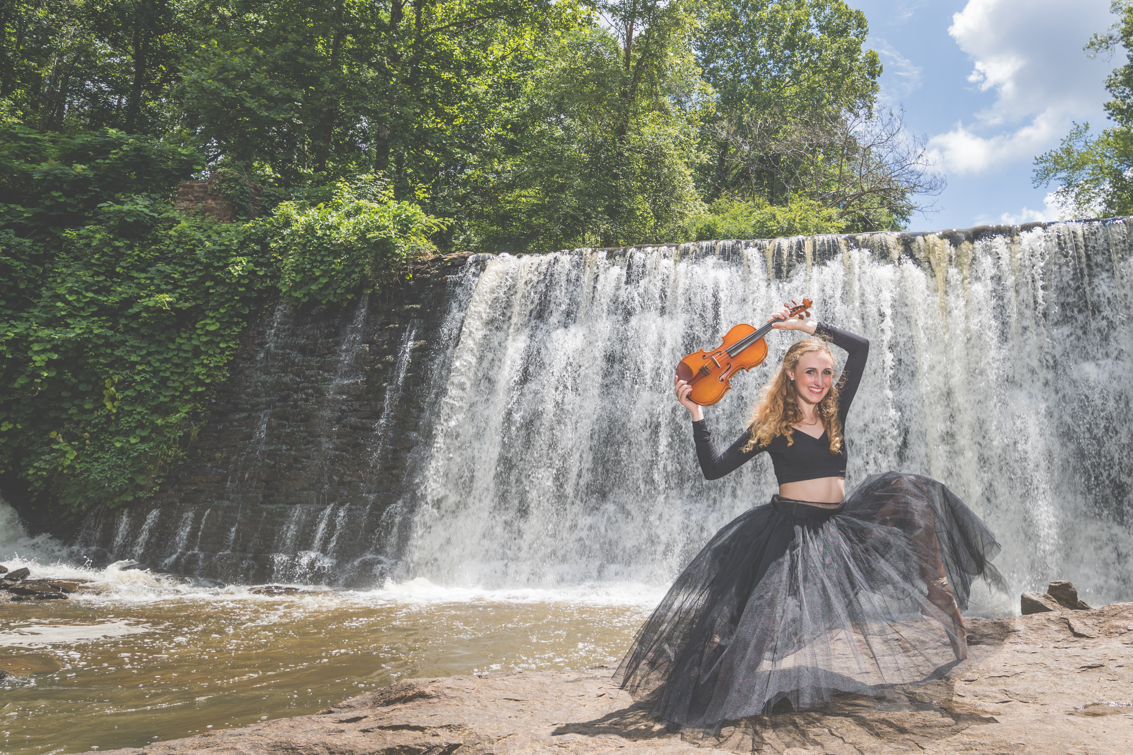 High school senior girl with her ballet pointe shoes and violin in front of Roswell Mill dam