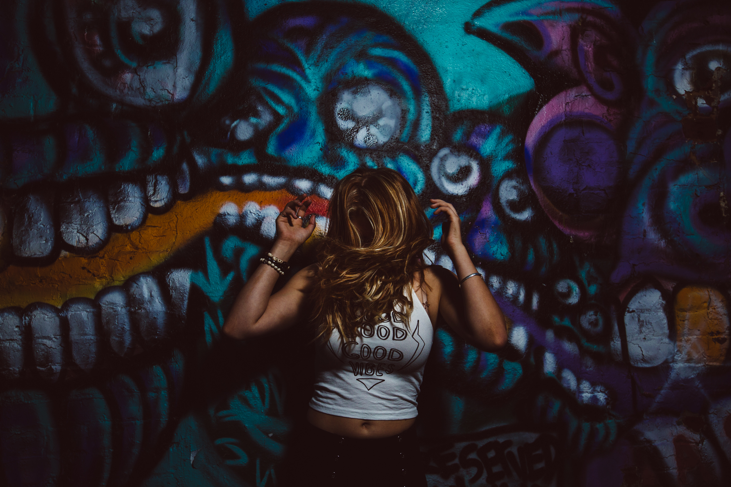 Atlanta high school senior girl dancing in front of grafitti wall wearing a shirt that says Good Vibes and her hair is flying in front of her face