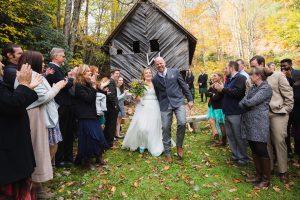 Atlanta destination wedding photographer captured Bride + Groom exiting ceremony with cheering guests in front of old Ashevill barn in the mountains