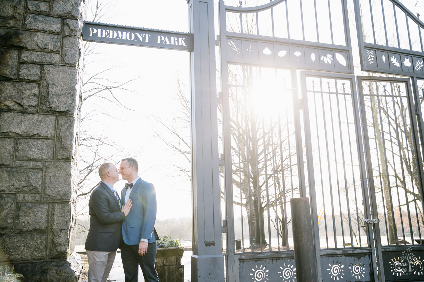 Two men in suits touching noses under Piedmont Park gate
