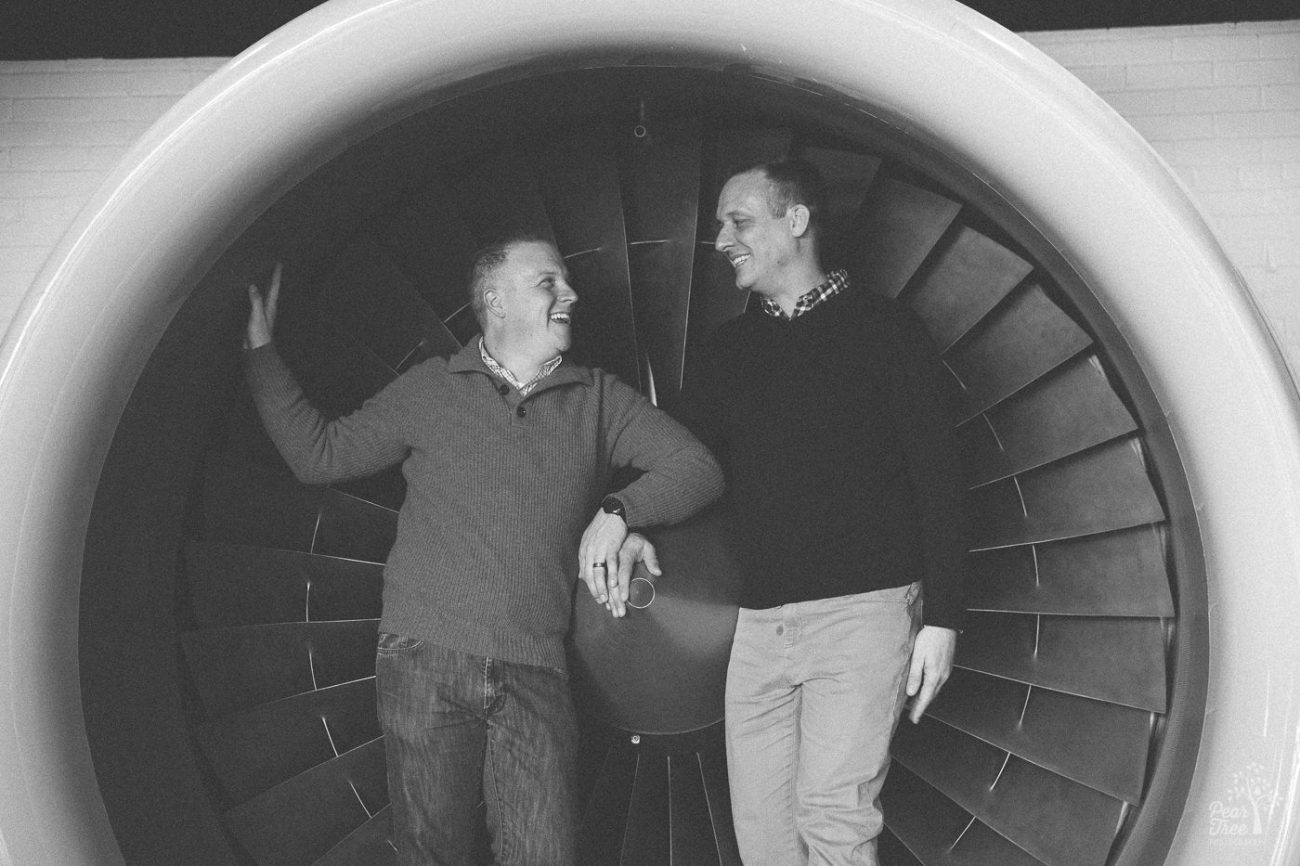 Two men standing inside of a jet engine and holding hands.