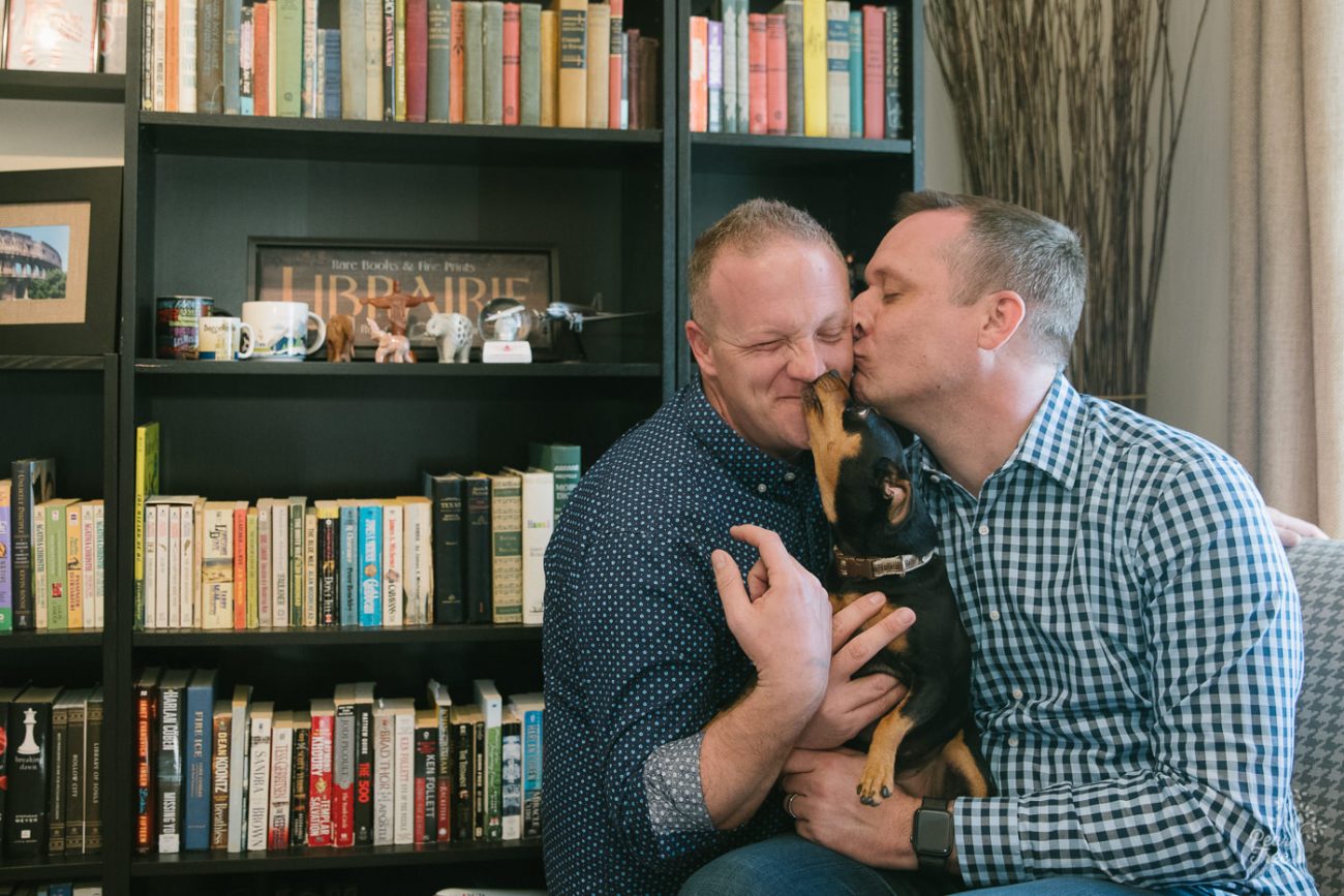 Two men kissing each other and getting their faces licked by their minpin