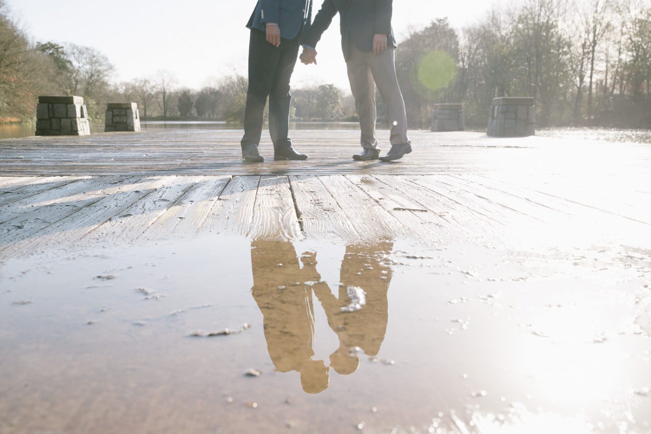 Reflection of two men almost kissing while holding hands on Piedmont Park dock.