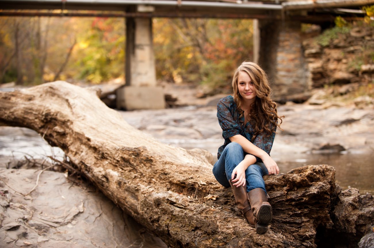 High school senior girl sitting on fallen tree at Sope Creek