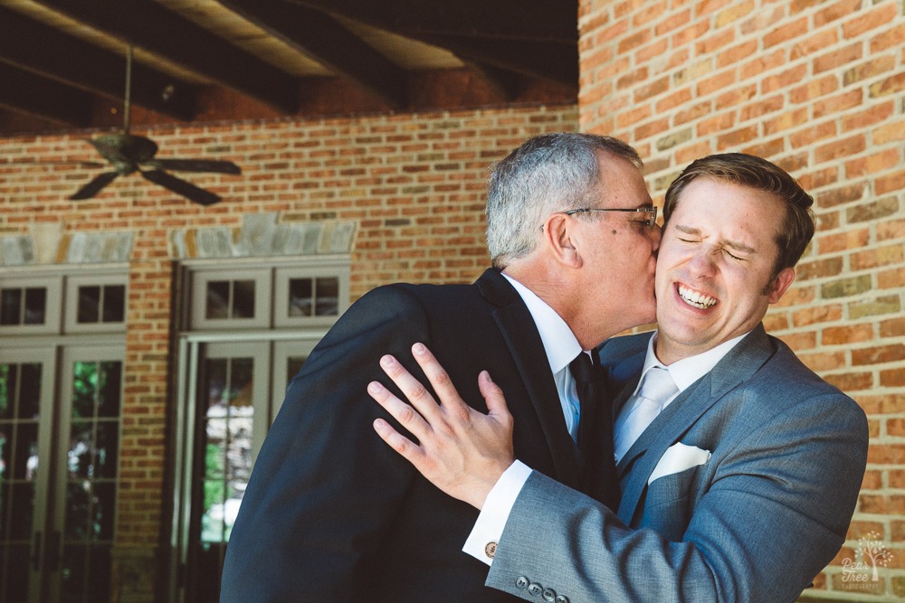 Groom laughing as his dad kisses his cheek.