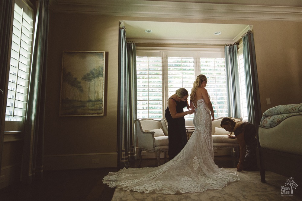 Sister and mother helping fasten bride's dress.