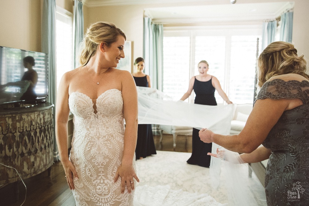 Sister and mom holding cape out from top of bride's dress.