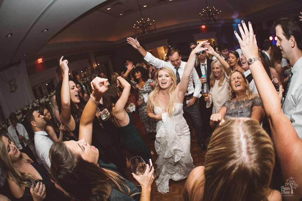 Bride dancing and singing with hands in the air surrounded by friends and mom.