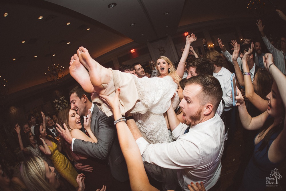 Bride crowd surfing in wedding reception as other dance or document on snapchat and facebook live.