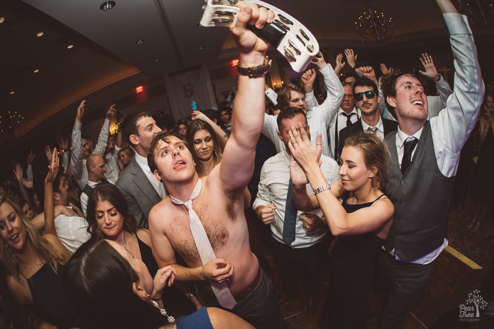 Groom dancing in wedding reception and raising tambourine in the air.