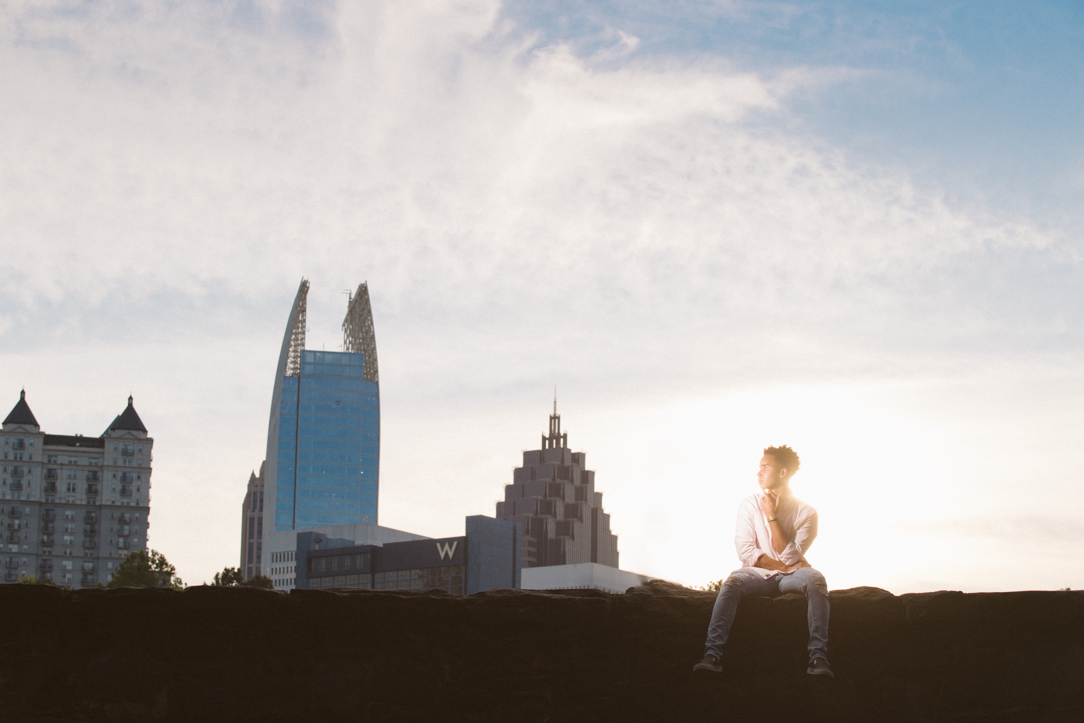 African American senior boy sitting on wall in front of Atlanta skyline at sunset