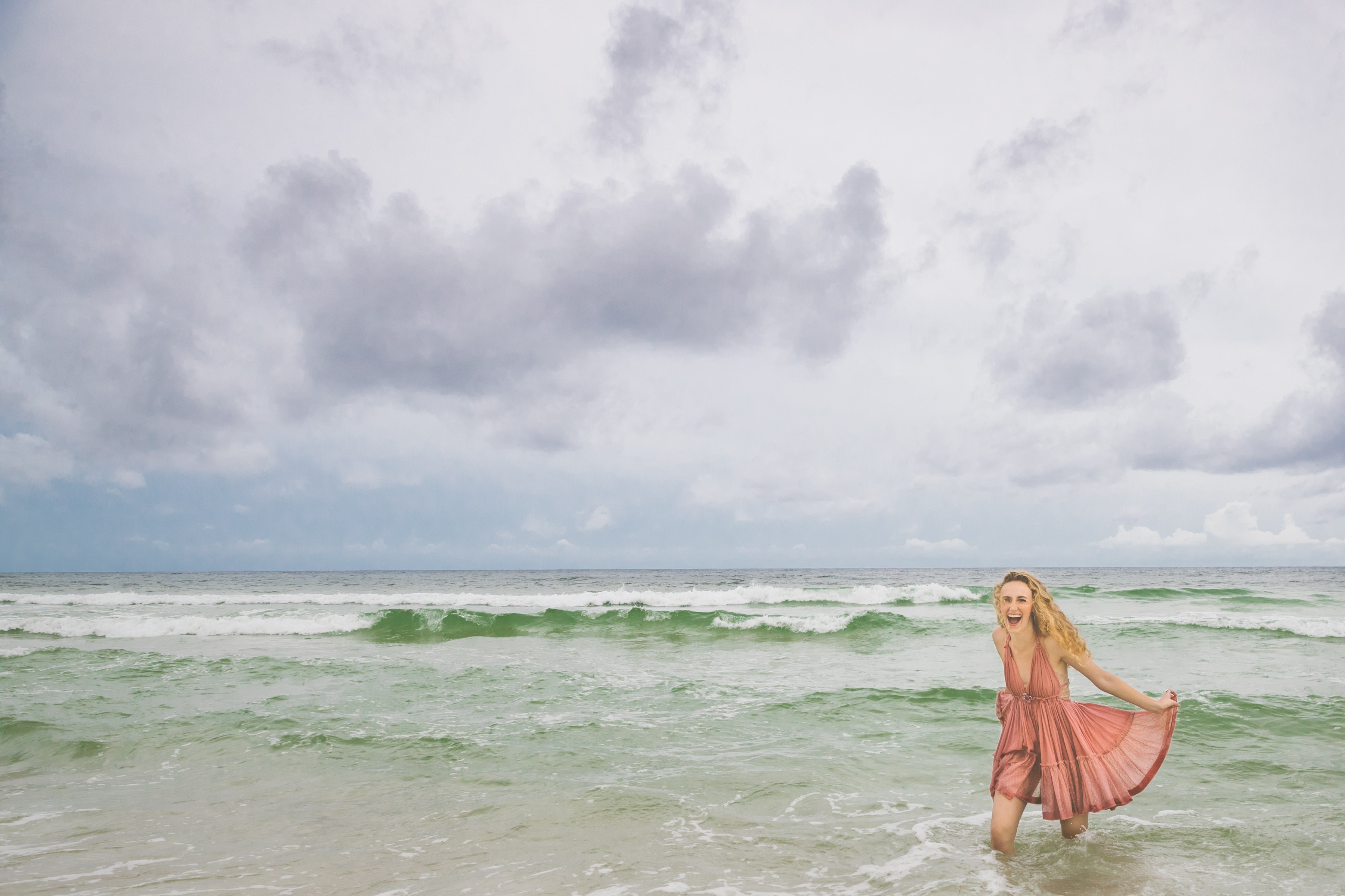 High school senior walking out into the emerald Gulf of Mexico with stormy skies