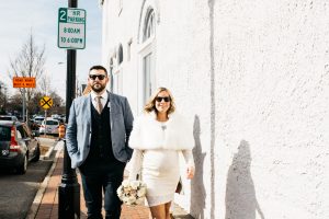 Smiling pregnant bride walking through downtown Marietta square with her husband and both wearing sunglasses