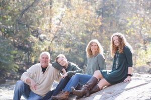 Happy parents sitting with their teenagers on boulder in woods