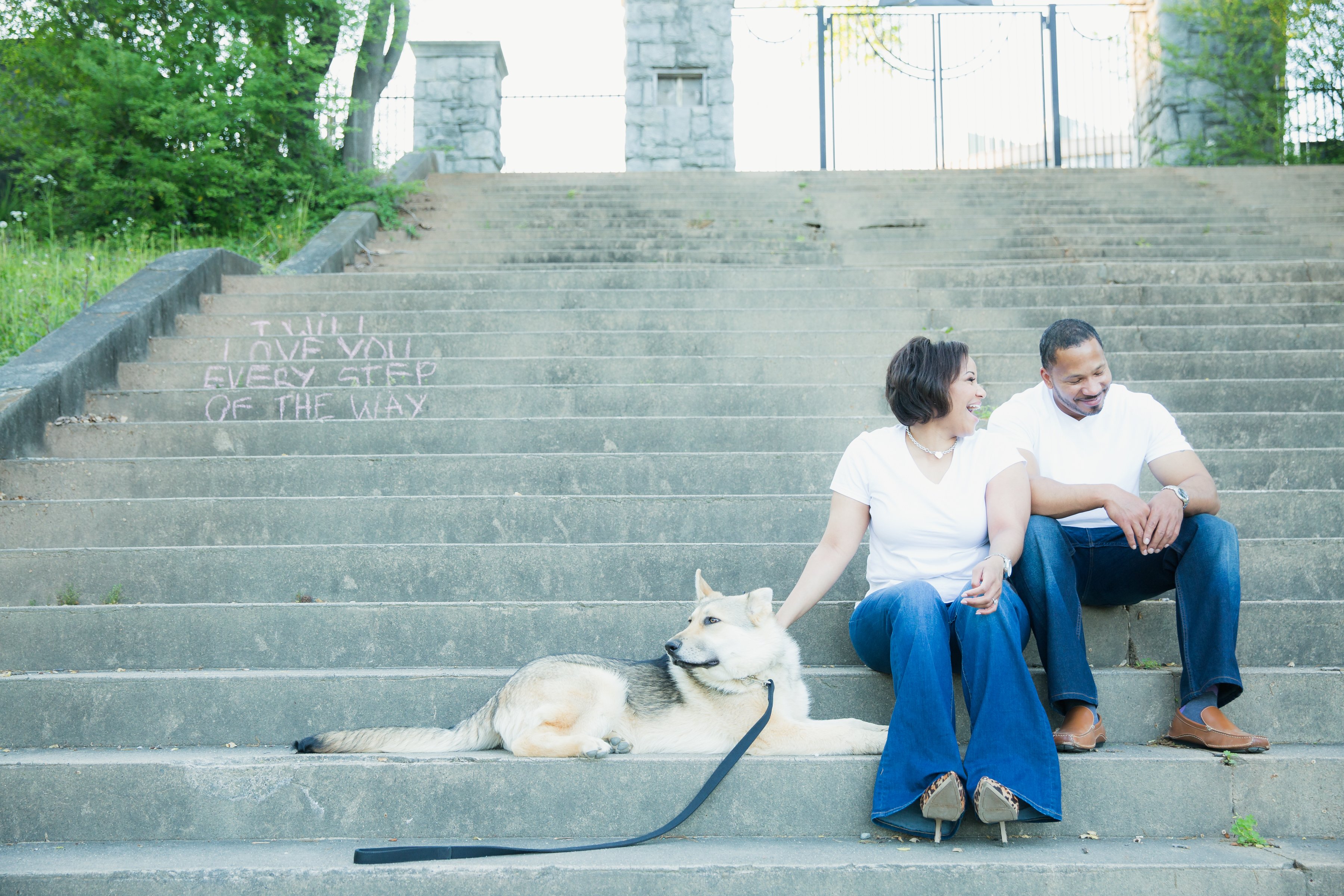 Happy engaged couple sitting on Piedmont Park steps with their German Shepherd