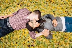 A couple laughing and kissing each other while laying in golden gingko leaves on the ground