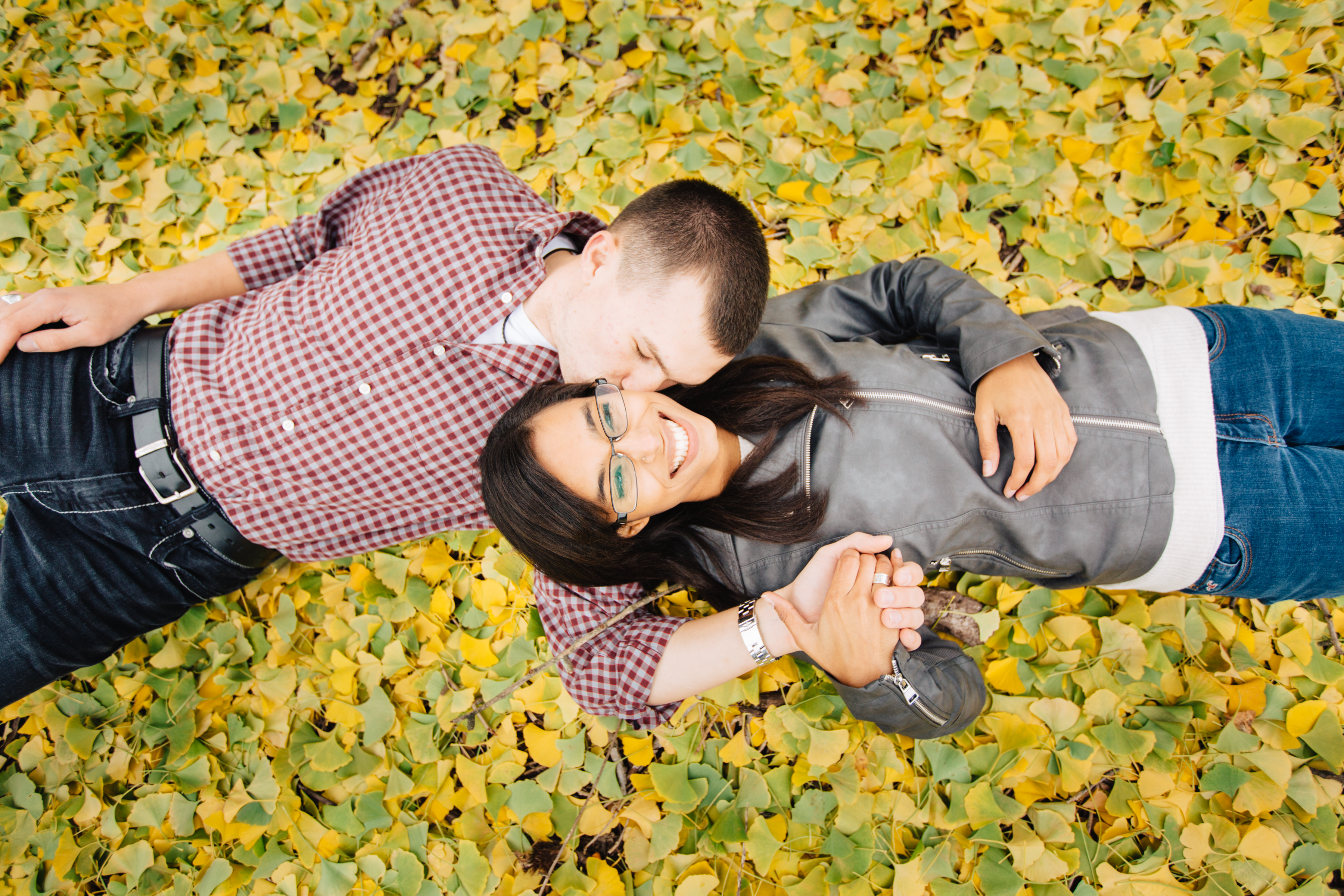 Happy couple snuggling and laughing on a bed of golden gingko leaves