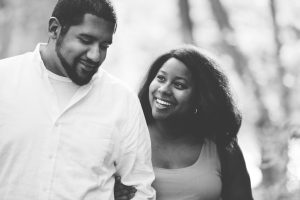 Black + white image of engaged couple walking arm in arm and smiling