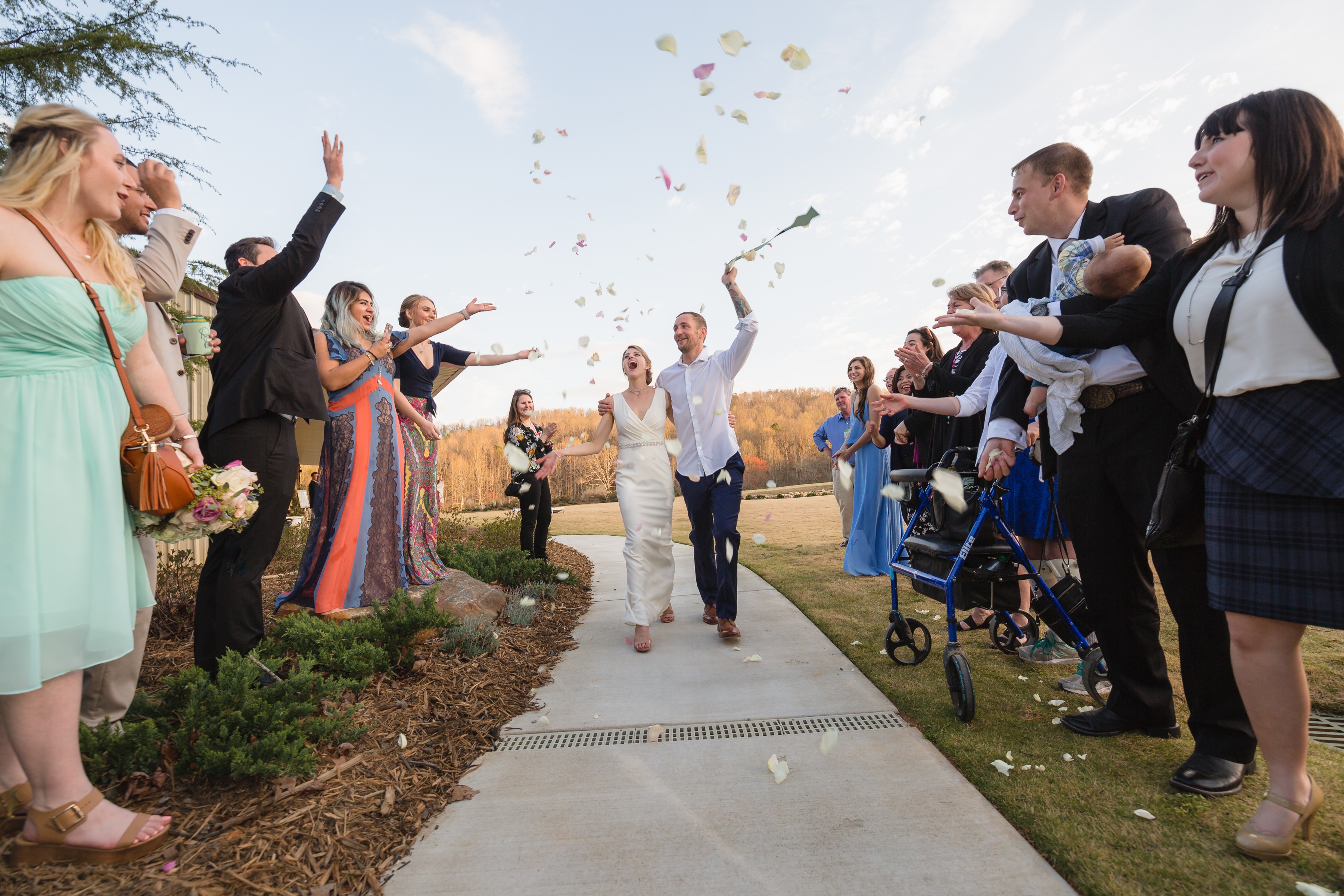 Bride + Groom exiting Greystone Estate laughing while friends and family cheer + throw rose petals in front of Atlanta documentary wedding photographer