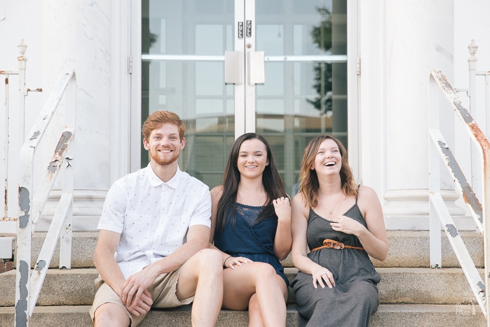 Three teenage and twenty something siblings smiling and laughing while sitting on steps together