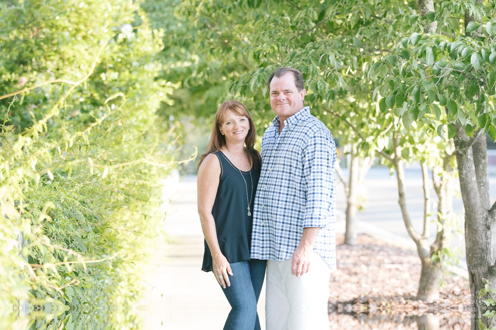 Jenna and Arnie Seyden standing close and smiling on a sidewalk surrounded by green crepe myrtles.