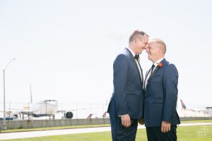 Two grooms standing close and smiling in front of Delta jets at Atlanta Hartsfield-Jackson airport