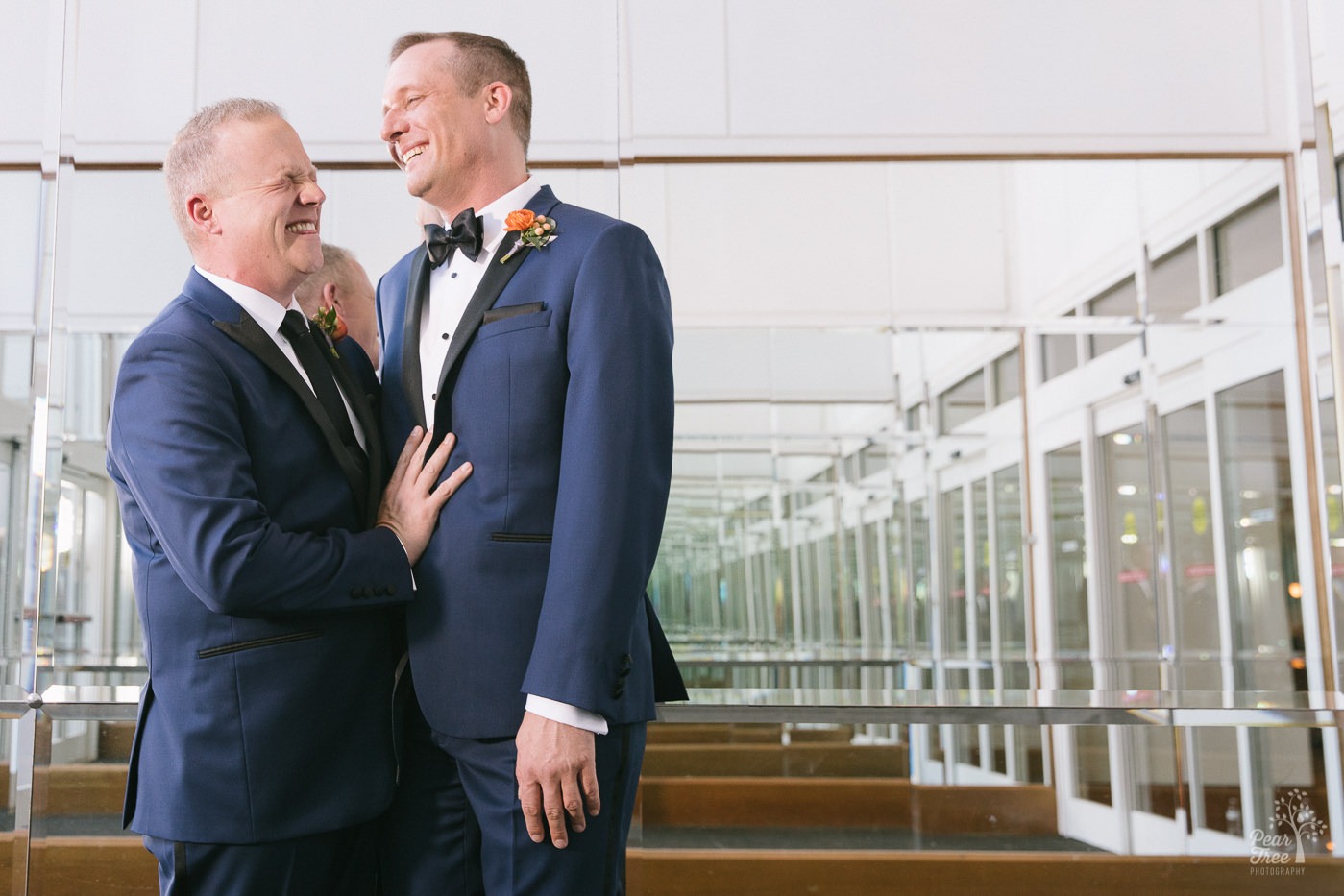 Two grooms laughing inside Renaissance Concourse Atlanta lobby of mirrors.