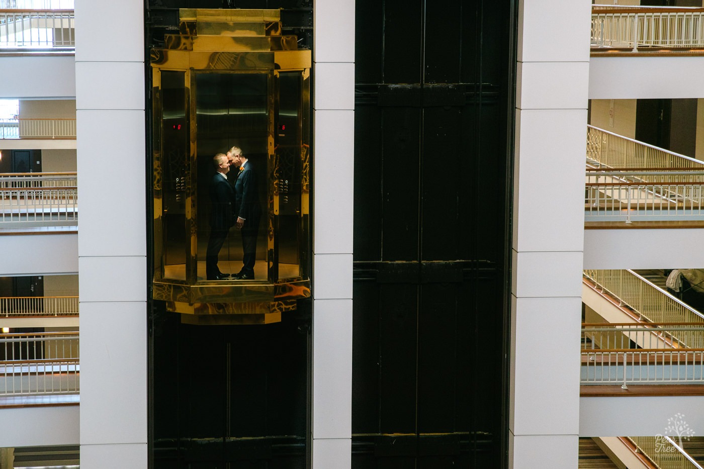 Two grooms facing each other, holding hands, and touching foreheads inside Renaissance Concourse Atlanta Airport Hotel elevator.