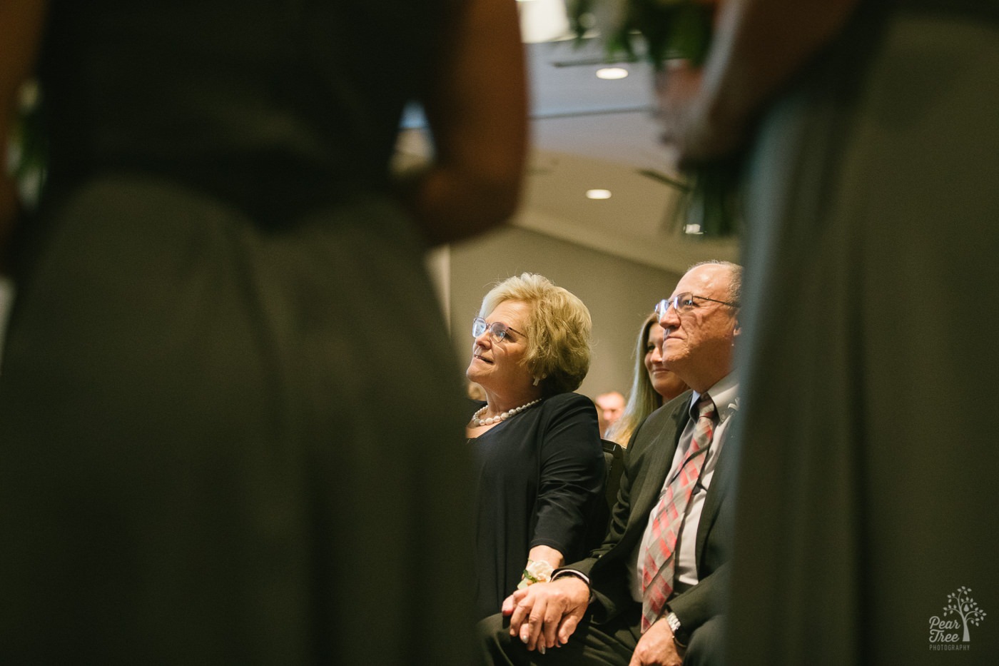 Groom's parents holding hands and smiling as they watch their son get married inside Renaissance Concourse Atlanta Airport Hotel.