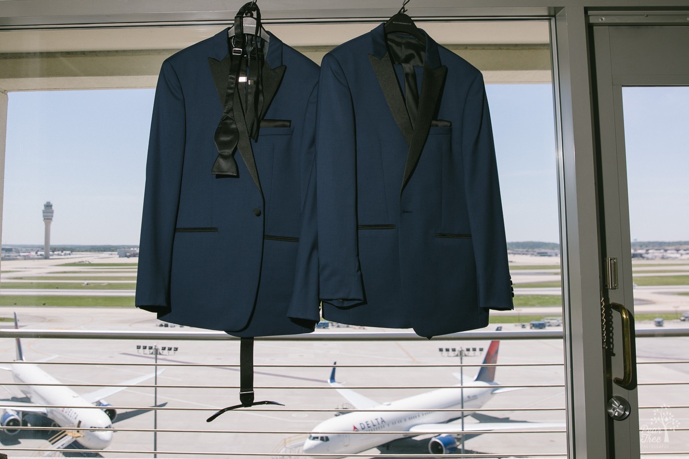 Two tuxes hanging in Atlanta Renaissance Concourse penthouse window overlooking Delta jets at Hartsfield-Jackson International Airport.