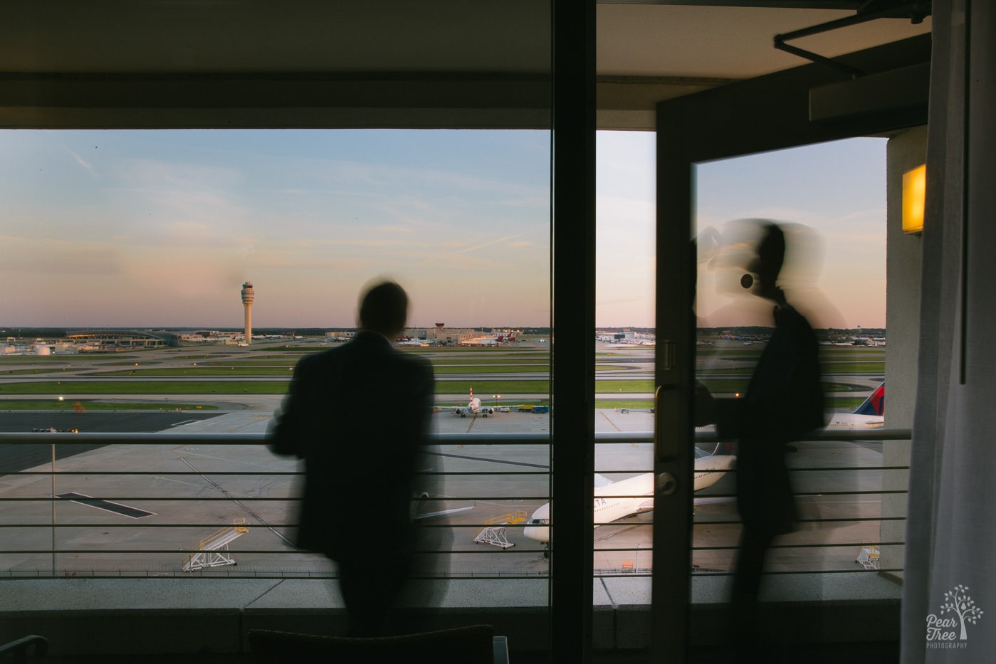 Silhouettes of two grooms on Renaissance Concourse Atlanta Airport Hotel penthouse balcony overlooking Hartsfield runways with Delta jets parked on the tarmac.