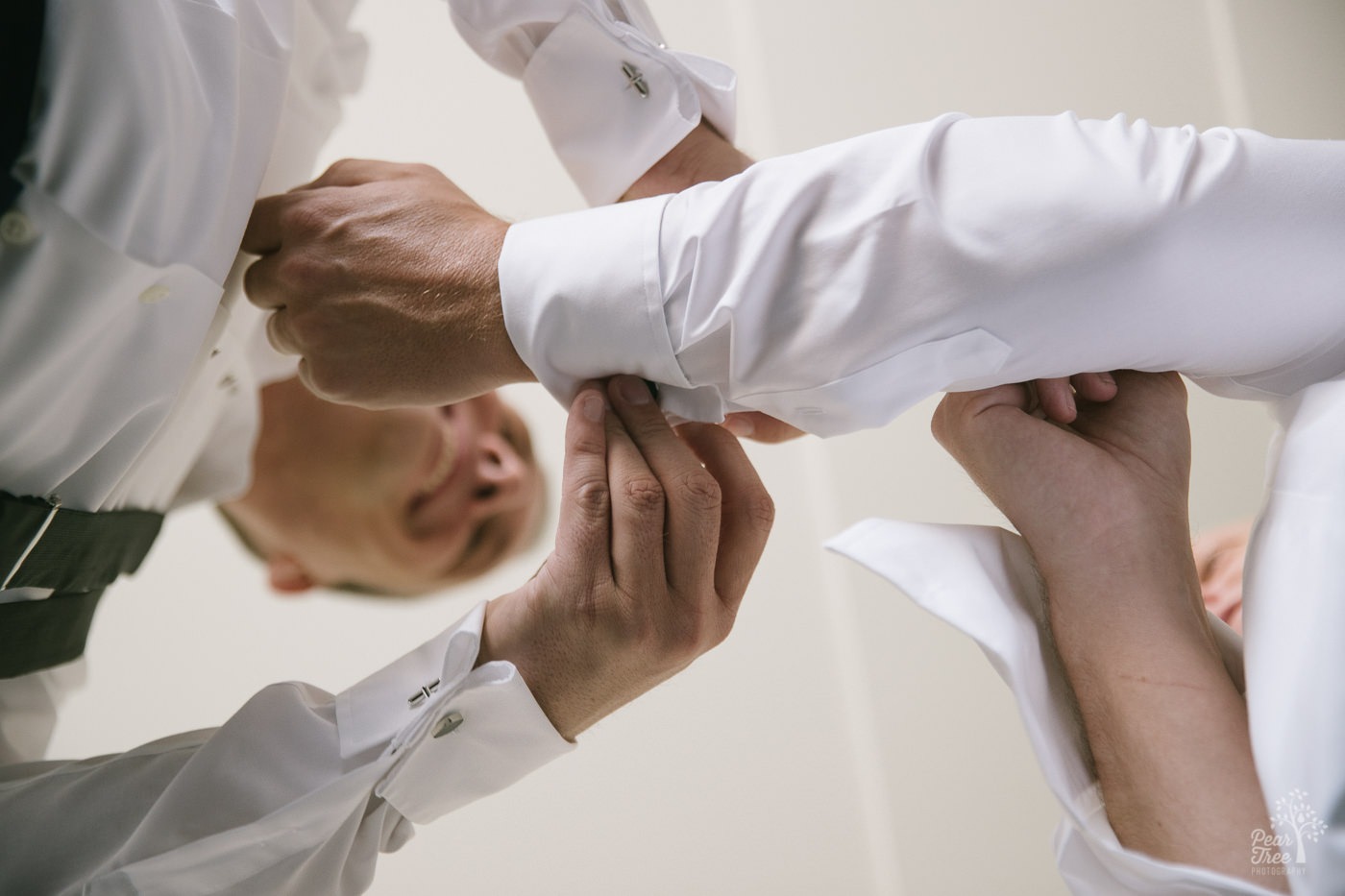 Looking up at two grooms helping each other with fastening cufflinks on their sleeves.