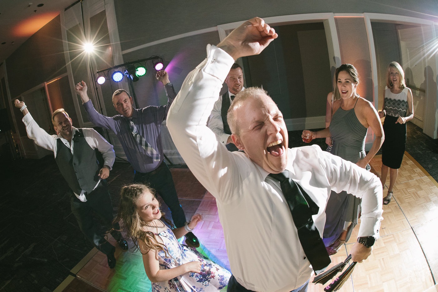 Groom dancing and laughing on dance floor.