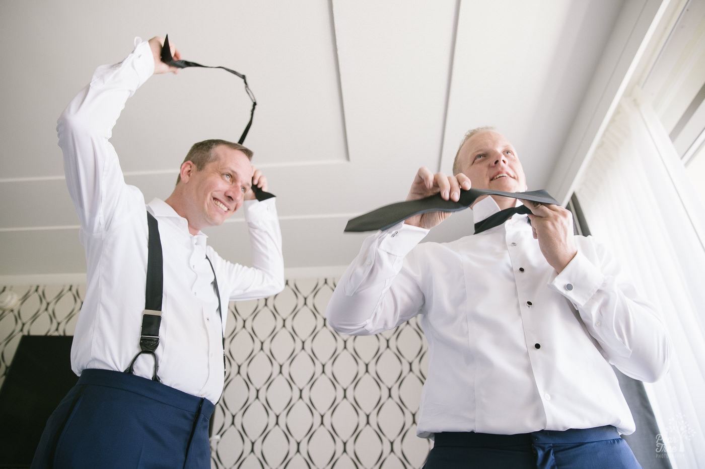 Looking up at two grooms getting dressed and putting on neckties for their wedding ceremony.