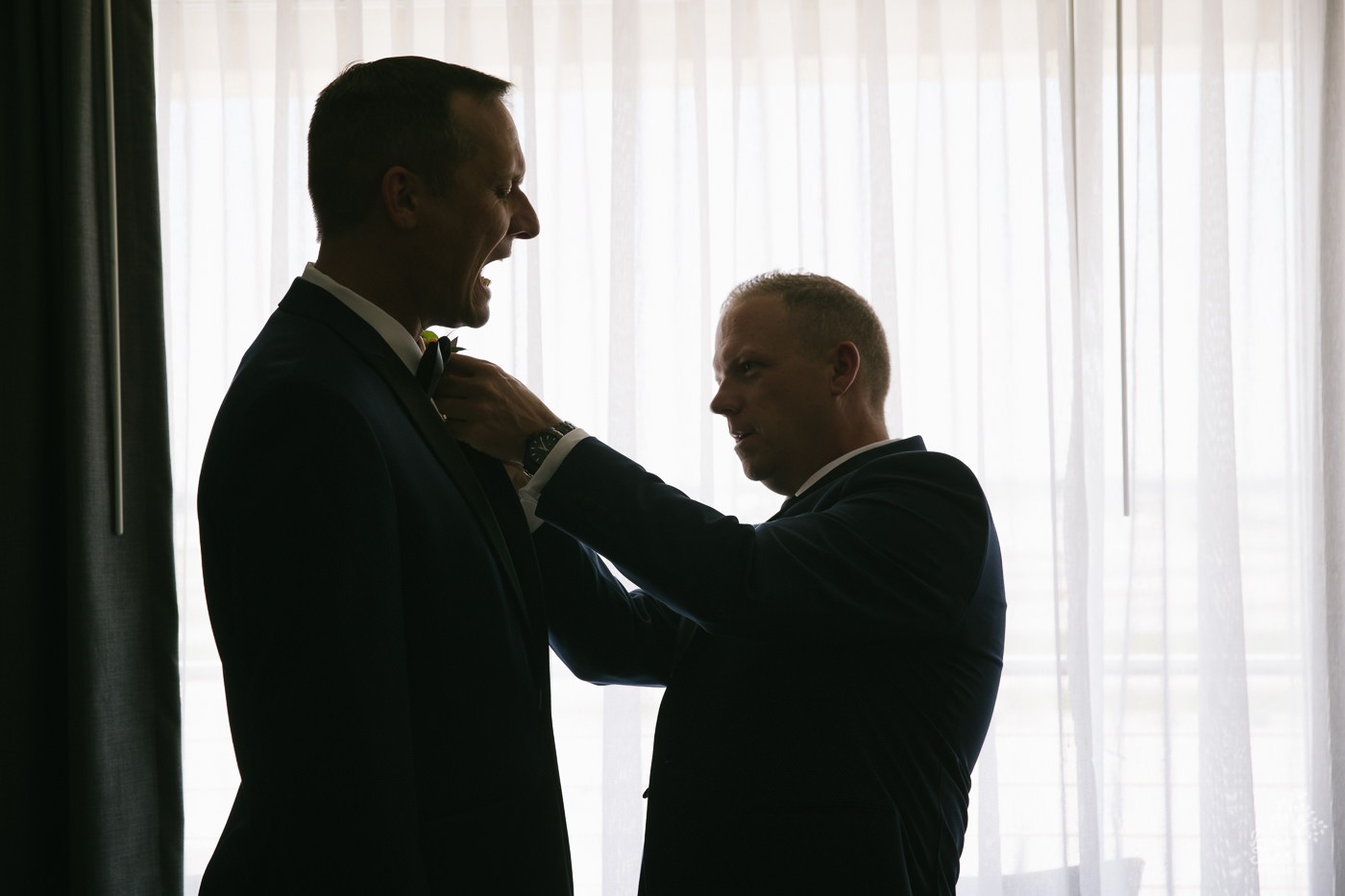 One groom pinning a boutonierre on his love's lapel and accidentally poking him.