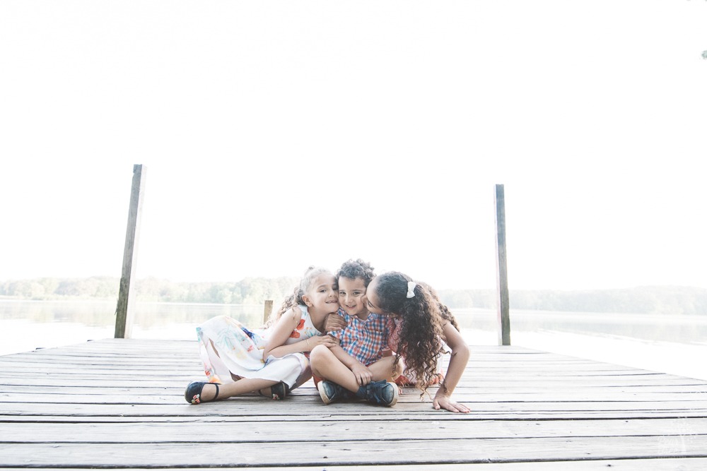 Two big sisters hugging and kissing their little brother at Lake Acworth.