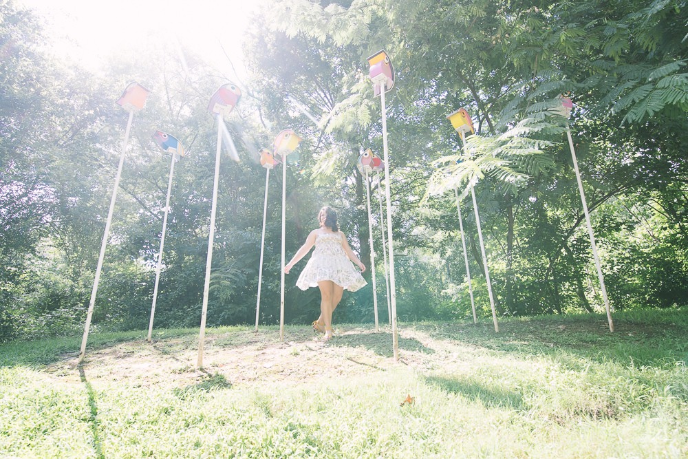 High school girl twirling in between bird houses as the sun makes her spinning dress shine and glow.