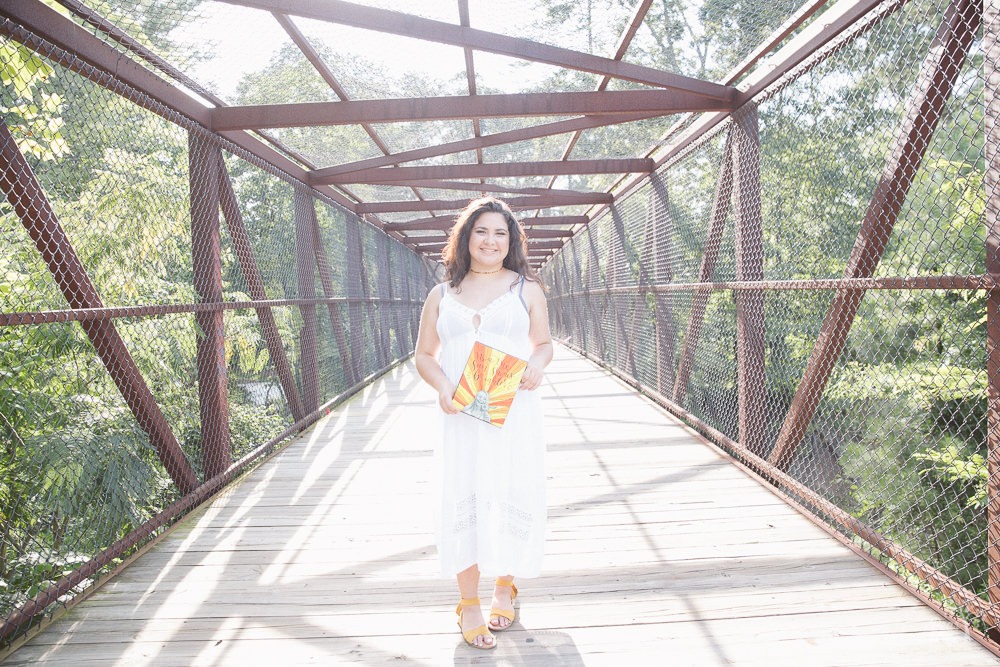 Woodstock High School senior holding #LiveLikeMaddie painting on a bridge in the sun.