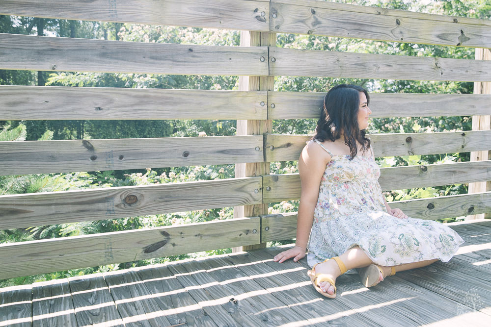 High school girl sitting on boardwalk in floral sundress.