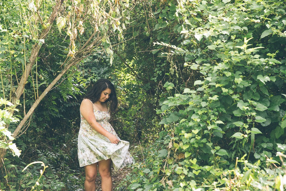 High school girl twirling her dress in the middle of a lush forest.