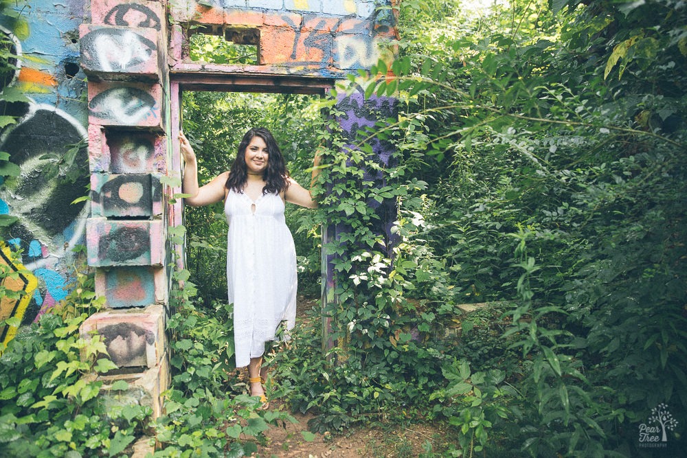 Teenage girl smiling and standing in the doorway of overgrown ruins.