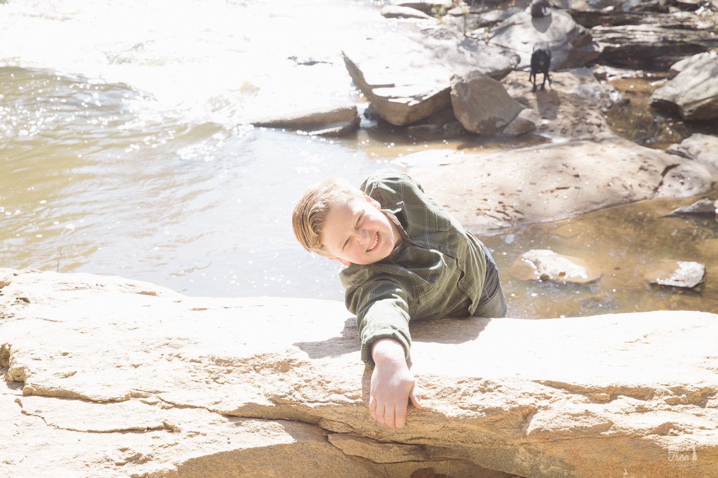 Teenage boy pretending to hang onto cliff by one hand far above the water of Sope Creek.