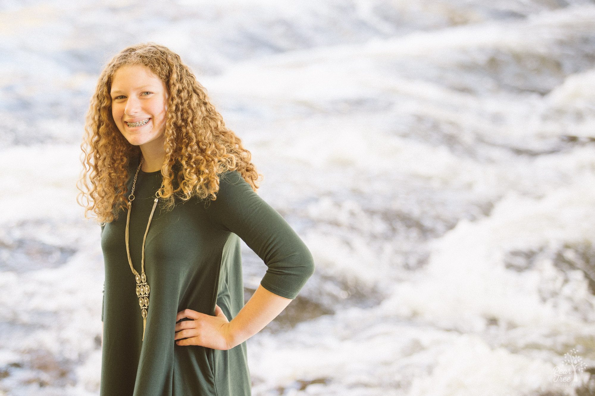 Teenage girl smiling and standing with hand on hip in front of Sope Creek rapids.