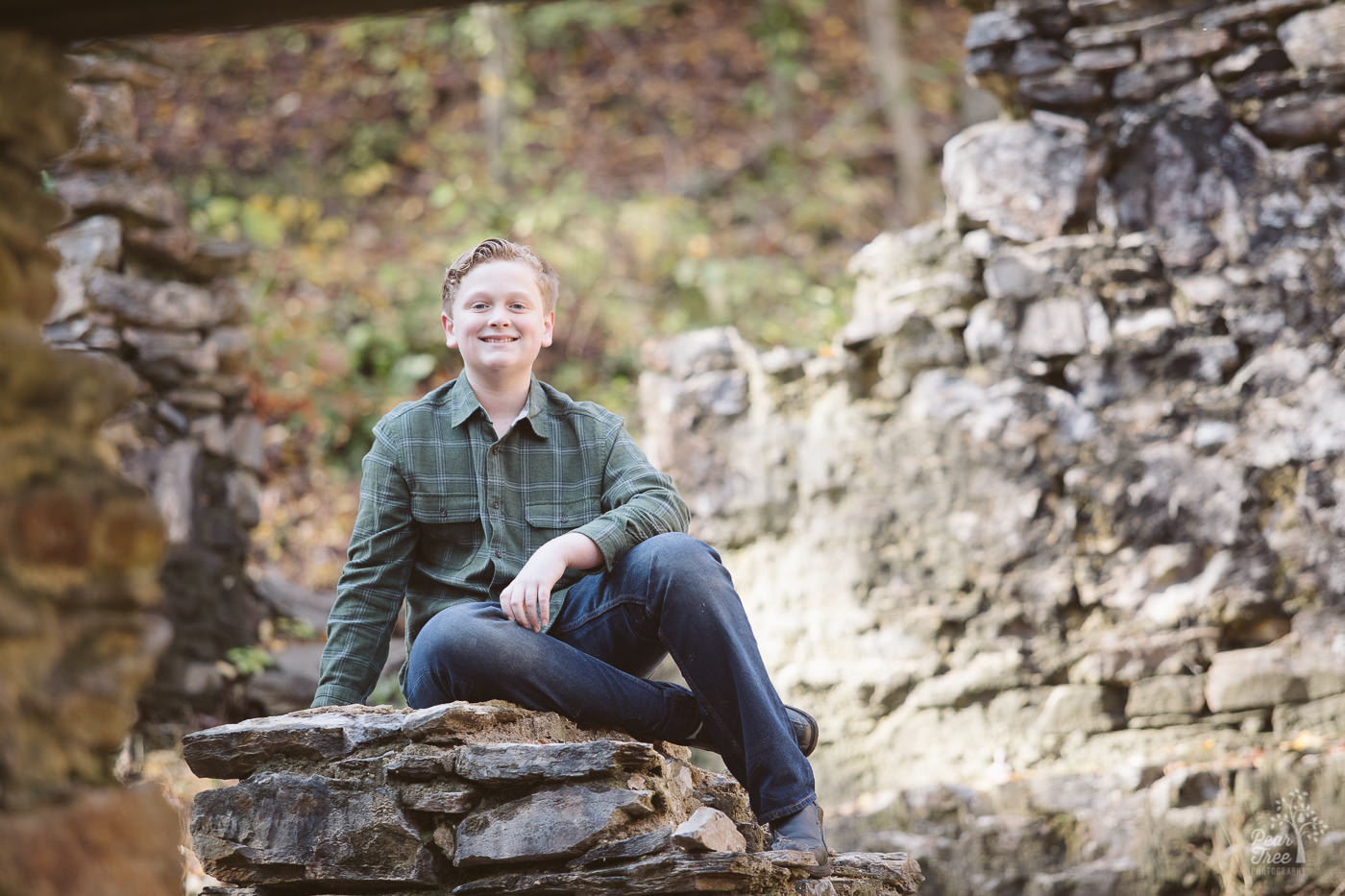 Teenage boy sitting tall on paper mill ruins and smiling big.