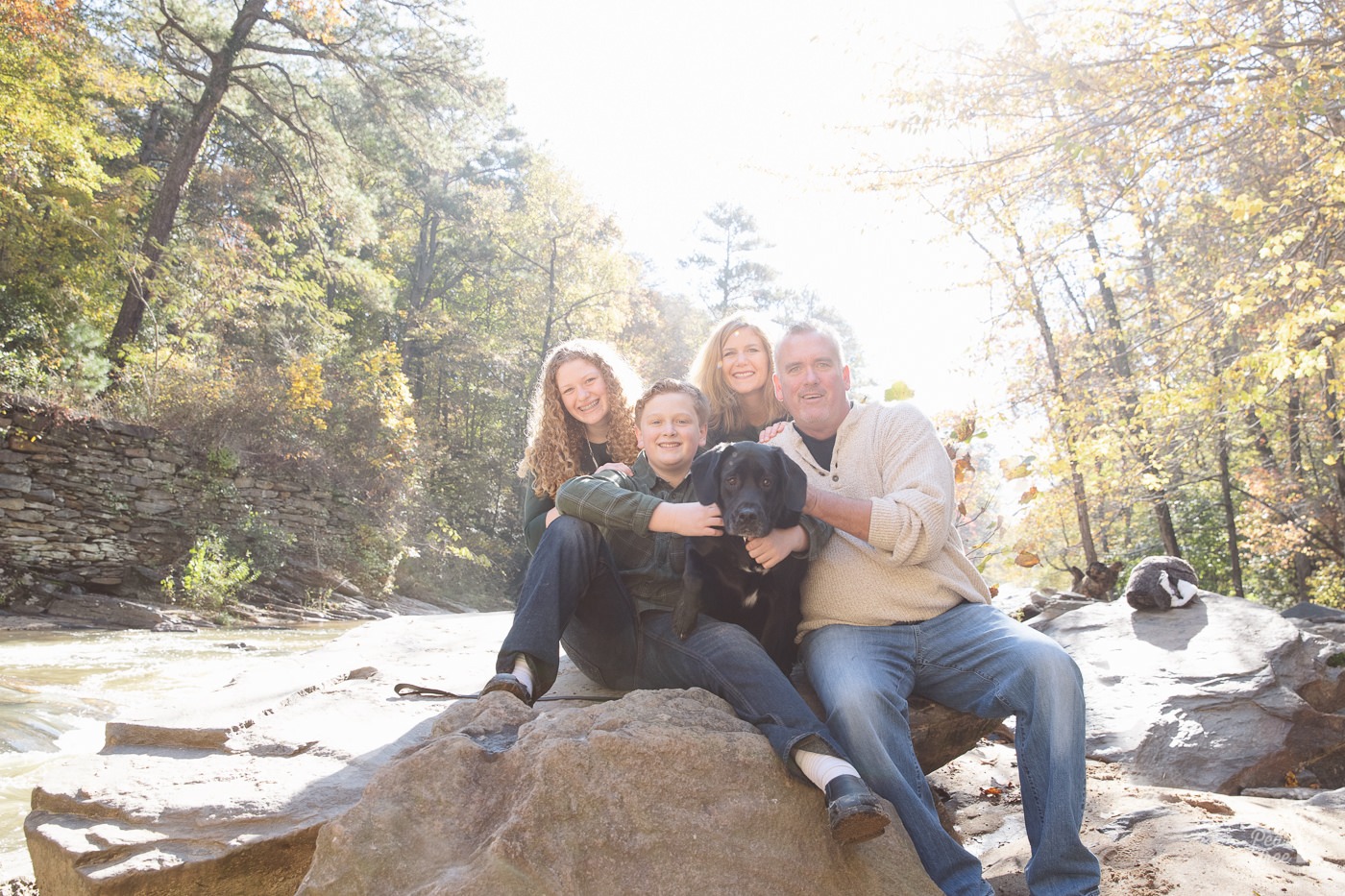 Family of four sitting on shoals with their black lab at Sope Creek.