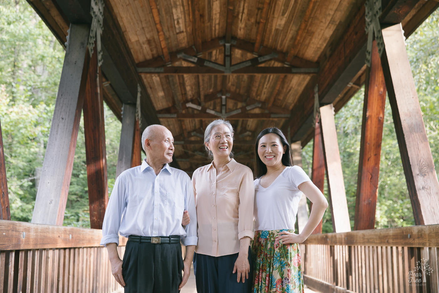 Proud Chinese parents standing in covered bridge at Roswell Mill with their adult daughter.